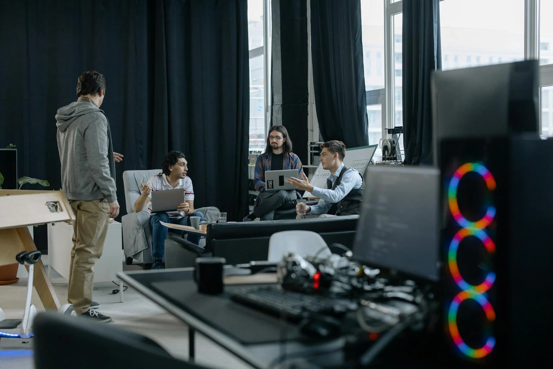 A group of professionals engaged in a casual meeting at a modern office, discussing projects on laptops and tablets.