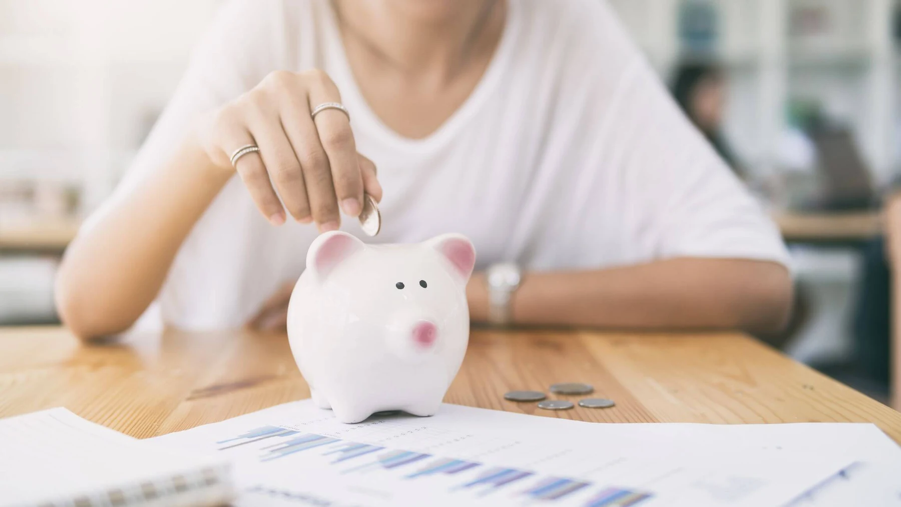 an image of a woman putting a coin in a white piggy bank